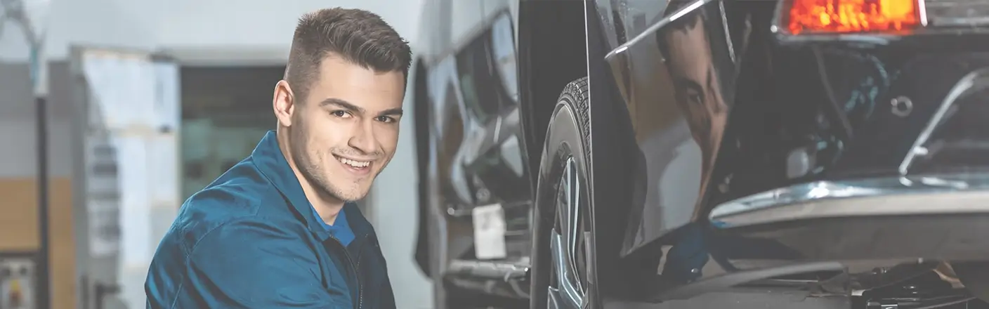 Förderung von Ausbildung und Weiterbildung im Kfz- und Vulkaniseur-Handwerk Lächelnder Automechaniker in blauer Arbeitskleidung neben einem Auto in einer Werkstatt